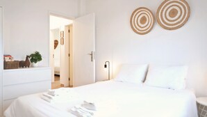 Un letto rifatto con lenzuola e asciugamani bianchi, un comodino con una lampada e due decorazioni circolari a parete.