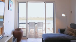 Una stanza con un letto, una scrivania con un computer, un vaso grande e vista su un patio esterno con sedie e un tavolo.