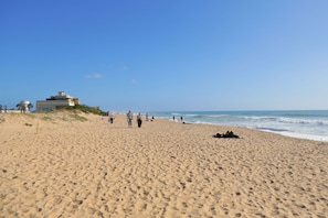 A sandy beach with footprints, a few people, and a building with a water tank on the left.