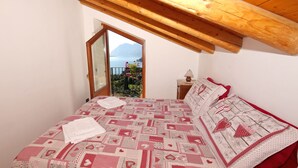 Un dormitorio con una colcha estampada, techo de madera y vista a un lago a través de una puerta abierta.