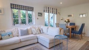 A living room with a white sofa, a small round table, and a dining area with striped chairs. - November Cottage (Dartmouth)
