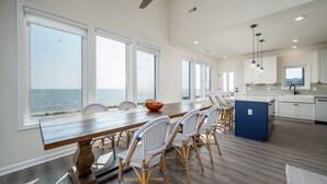 Uma cozinha espaçosa com uma mesa de madeira comprida, cadeiras de vime e vista para o oceano.