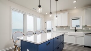 Uma cozinha moderna com uma bancada grande, armários brancos e vista para o exterior.