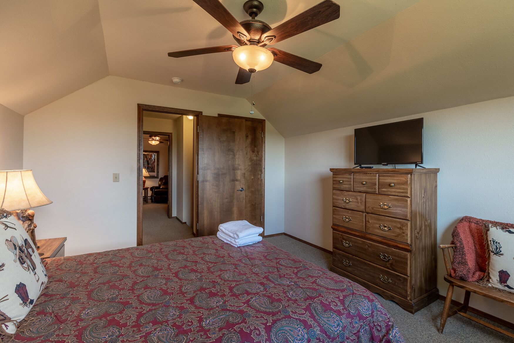 A bedroom with a bed, a wooden dresser, a television, and a ceiling fan.