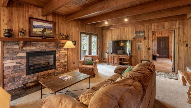 A cozy log cabin interior with a stone fireplace, wooden ceiling beams, a large TV, and a comfortable seating area. - Near Lake Hatcher and walk to San Juan Forest, Quiet Area. (Pagosa Springs)
