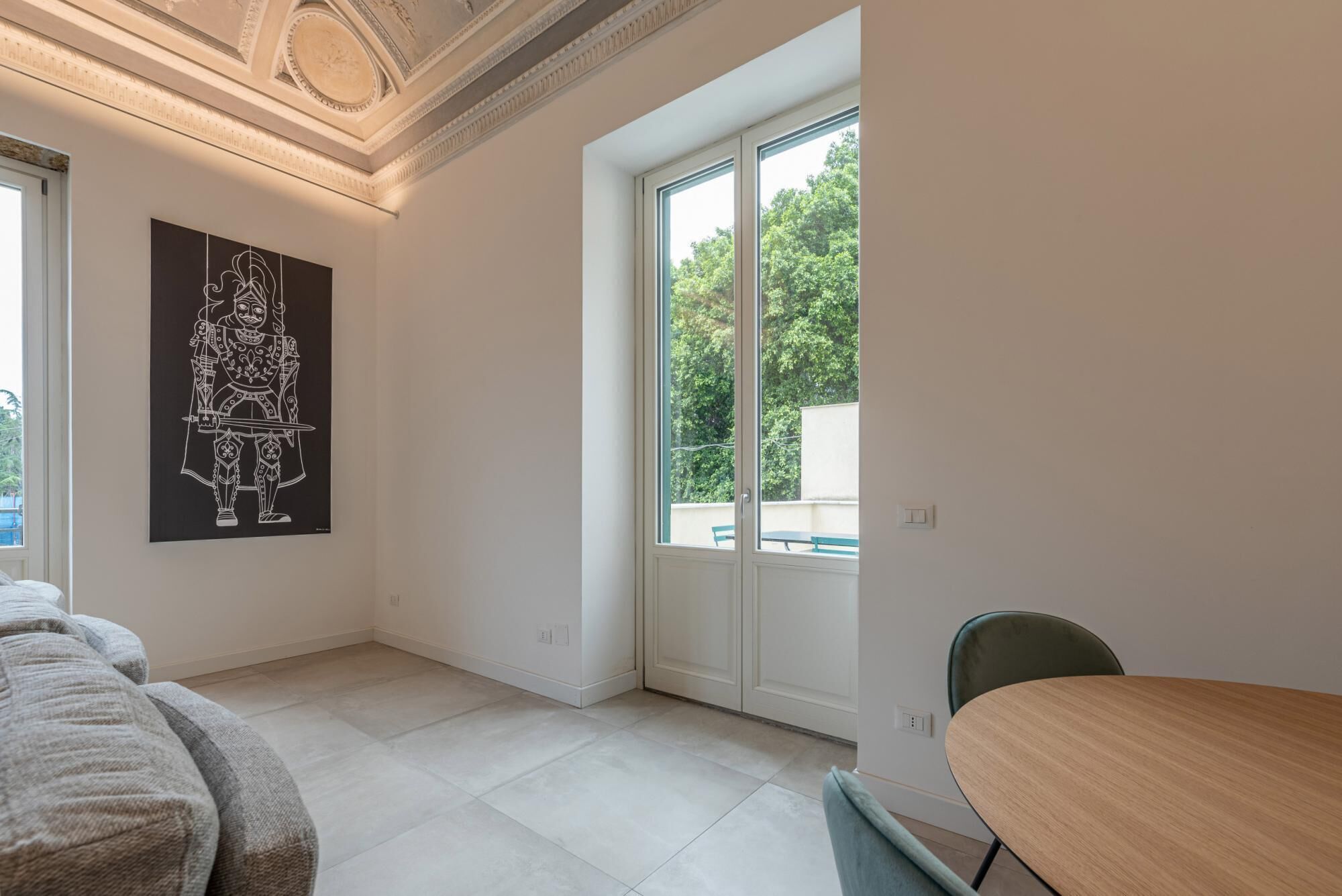 A modern room with a large window, a painting on the wall, and a dining area with a table and chairs.