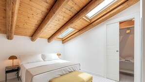 A bedroom with a sloped ceiling, a bed, a nightstand, and a bench. - Appartamento Principe di Camporeale con Terrazza (Palermo)