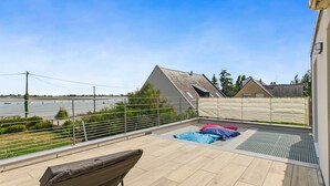 Een terras op het dak met uitzicht op een rivier, een overdekt zitgedeelte en een gebouw met een schuin dak.
