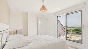 Een moderne slaapkamer met een groot bed, een nachtkastje, een lamp en uitzicht op een balkon met een stoel.
