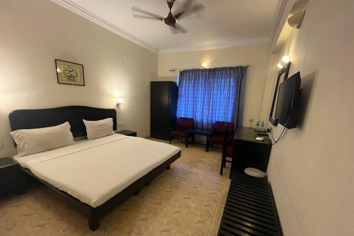 Quarto de hotel com cama, escrivaninha, cadeira, televisão e ventoinha no teto.