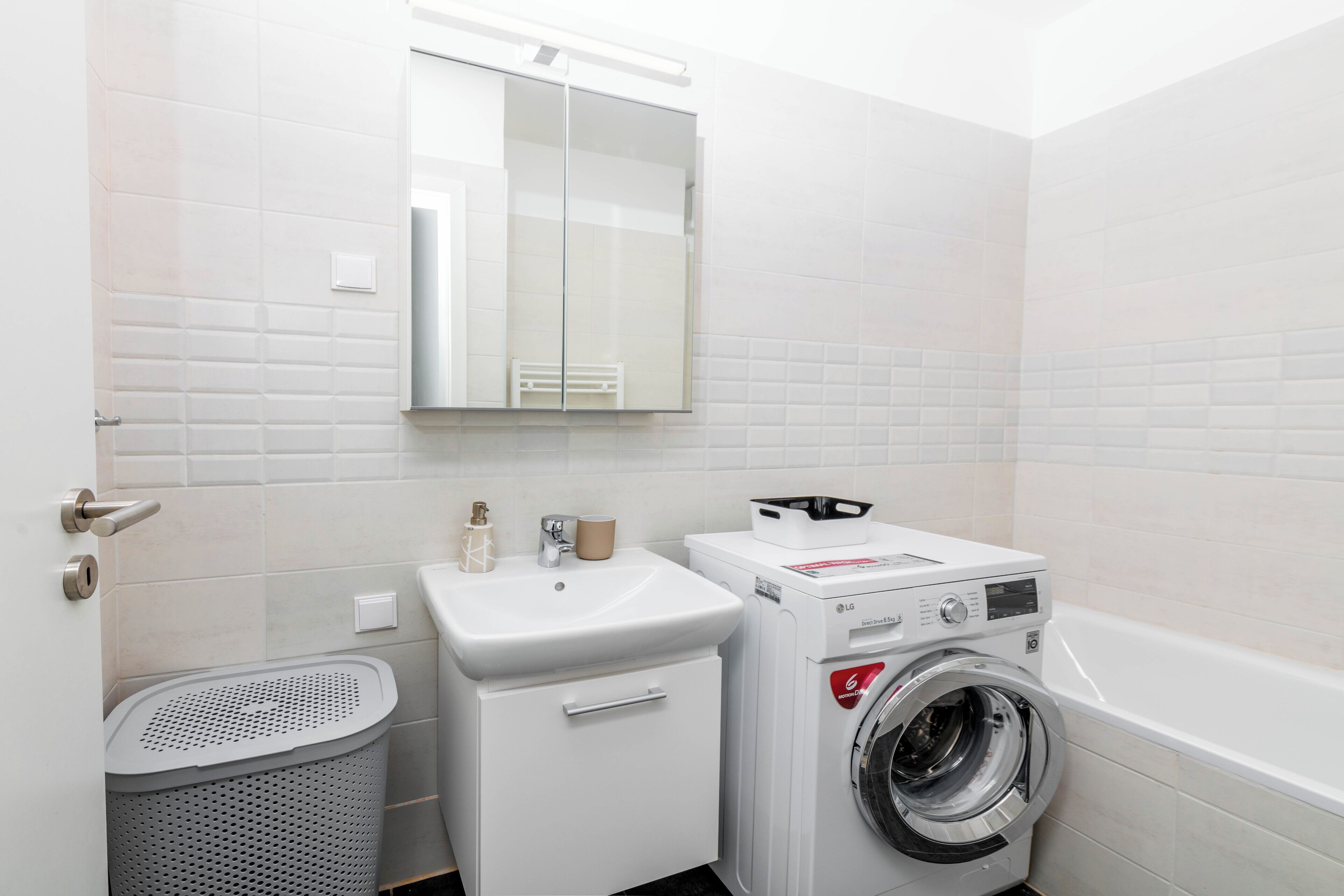 A compact laundry room with a washing machine, a sink, and a mirror.