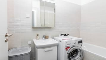 A compact laundry room with a washing machine, a sink, and a mirror.