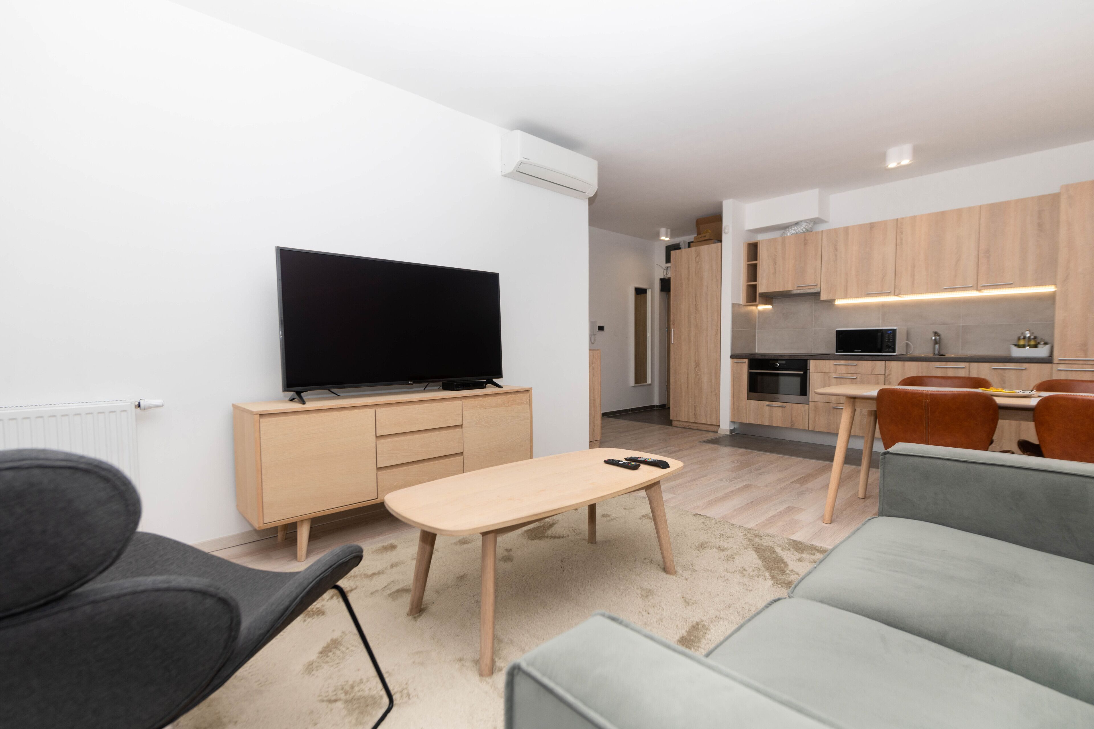 A modern living room with a flat-screen TV, a wooden coffee table, and a grey sofa.