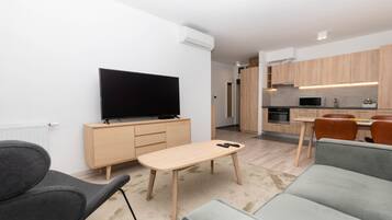 A modern living room with a flat-screen TV, a wooden coffee table, and a grey sofa.