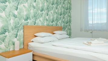 A neatly made bed with white bedding and pillows, a wooden headboard, and a nightstand with a white lamp.