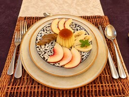 Un plato con rebanadas de manzanas, peras y plátanos, acompañado de una cuchara y un tenedor sobre un posavasos tejido.