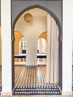 Un pasillo con suelo de baldosas, un arco de entrada y una lámpara colgante.