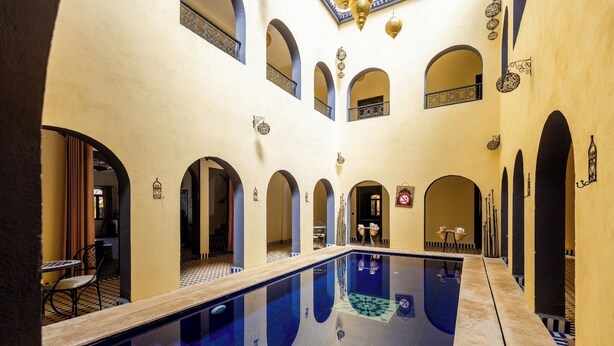 A pool with arched walkways and a ceiling with hanging lanterns. - Riad La Luna (Merzouga)