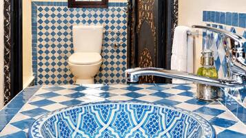 Un baño con un rebozado de azulejos blancos y azules a cuadros, un inodoro blanco, un lavamanos con una pileta de color azul estampada y una puerta dorada.