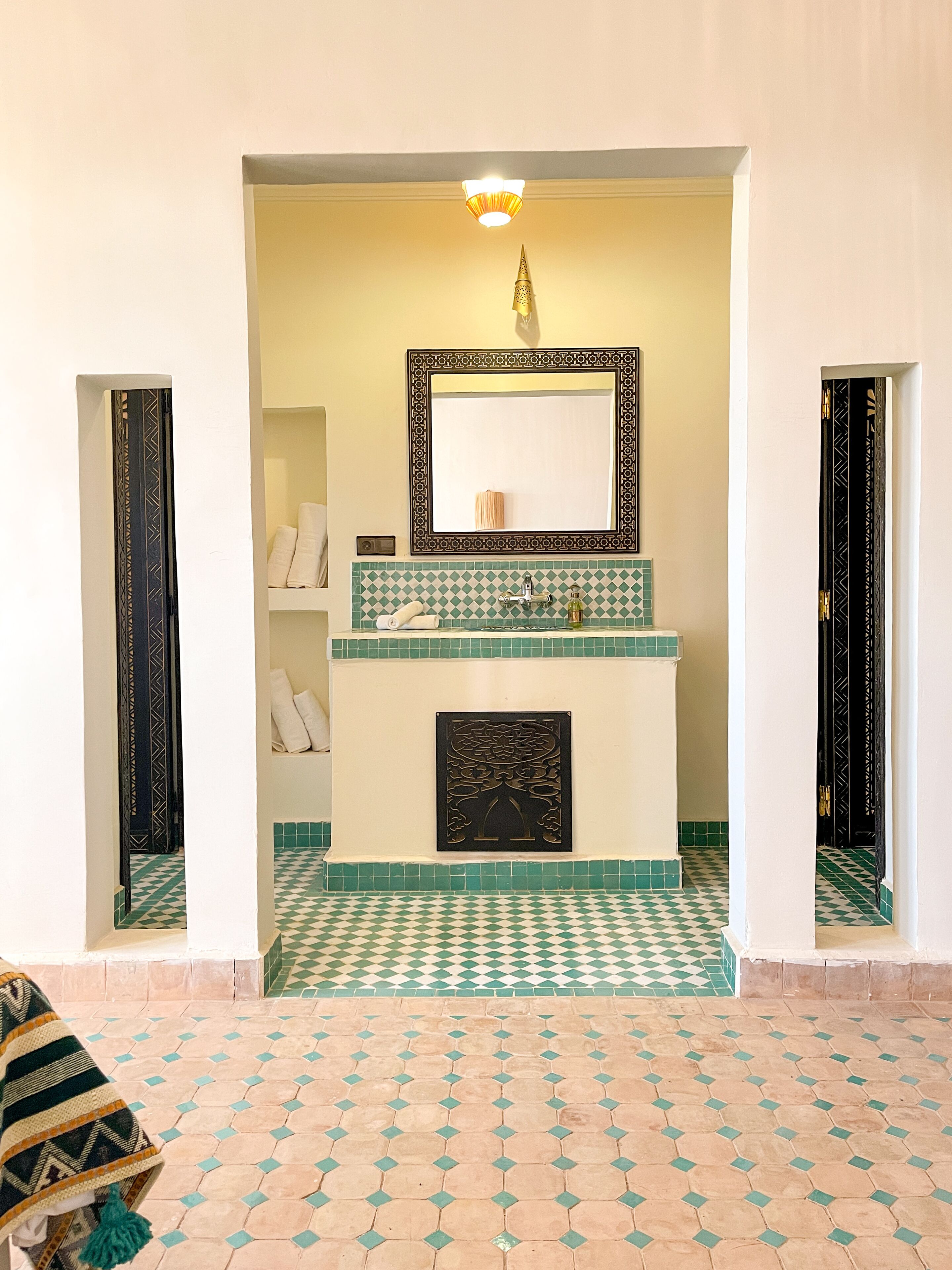 Un baño con piso a cuadros, zona de lavamanos con azulejos y un espejo con marco decorativo.