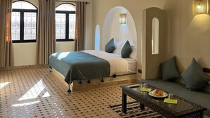 A hotel room with a bed, a sofa, a coffee table, and a patterned floor. - Riad La Luna (Merzouga)