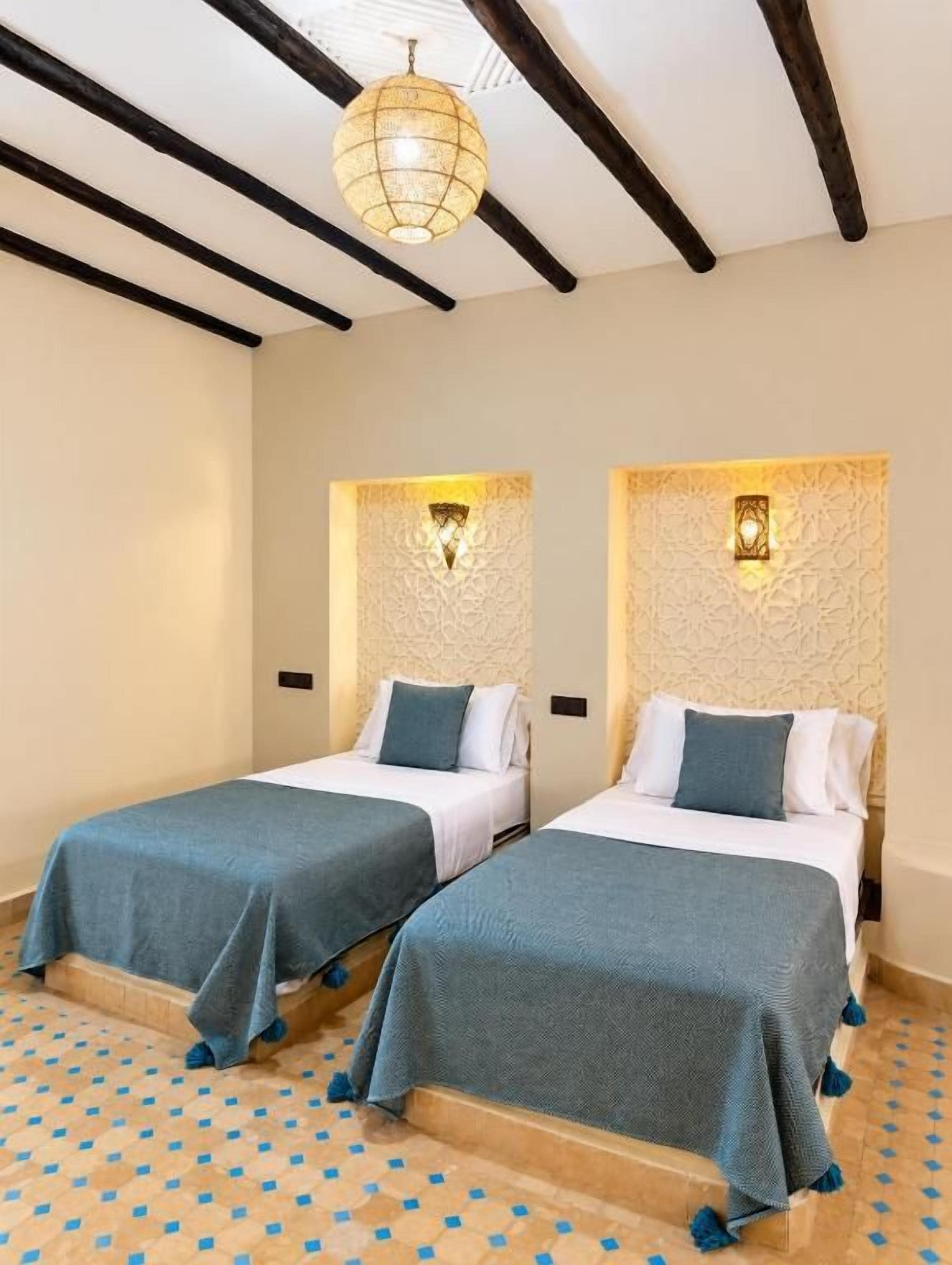 A hotel room with two beds, a patterned floor, and a hanging light fixture.