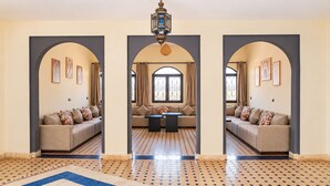A room with a sofa set, a dining table, and a patterned floor. - Riad La Luna (Merzouga)