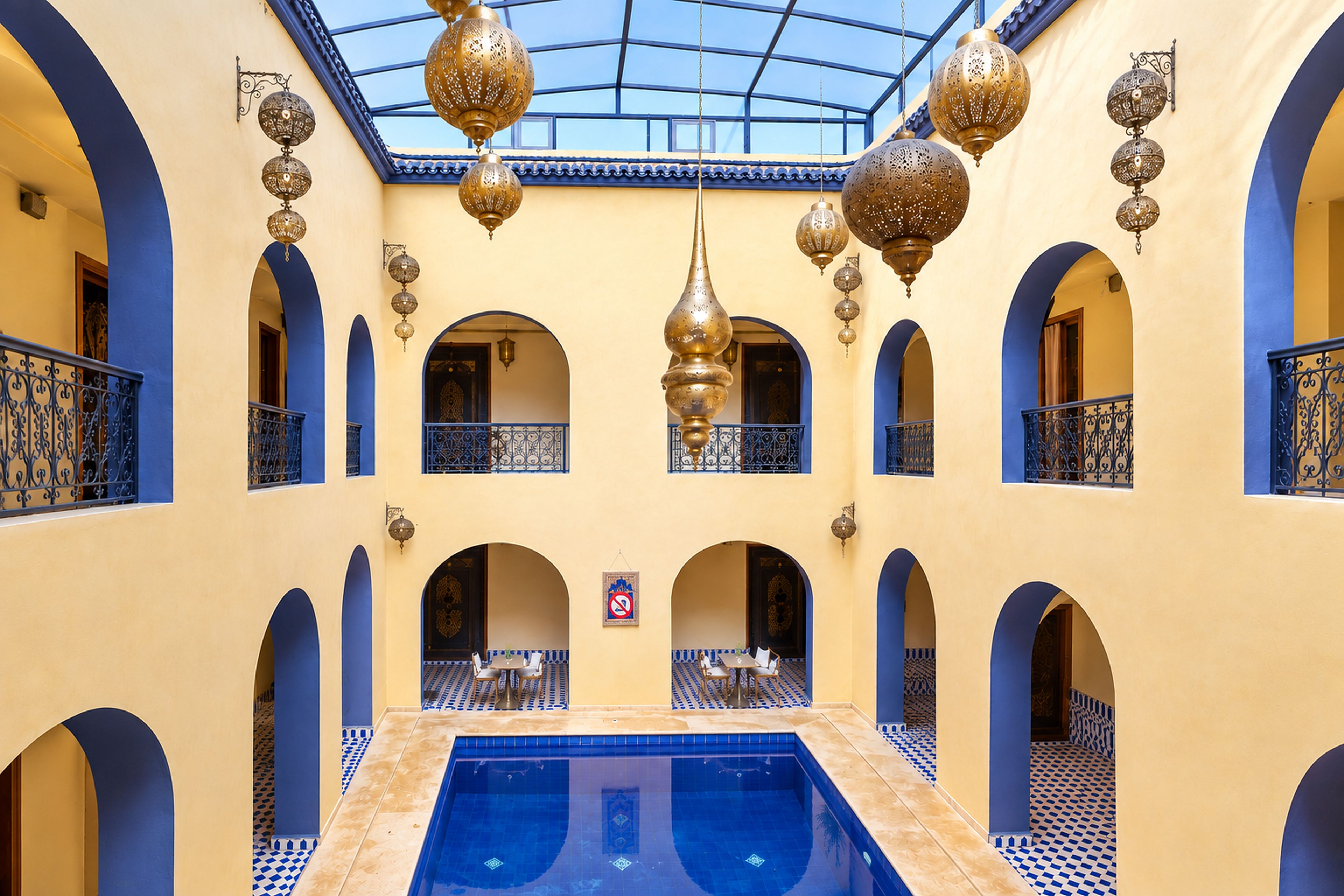 Un atrio de varios niveles con una piscina central, suelos con azulejos azules y elegantes faroles colgantes.