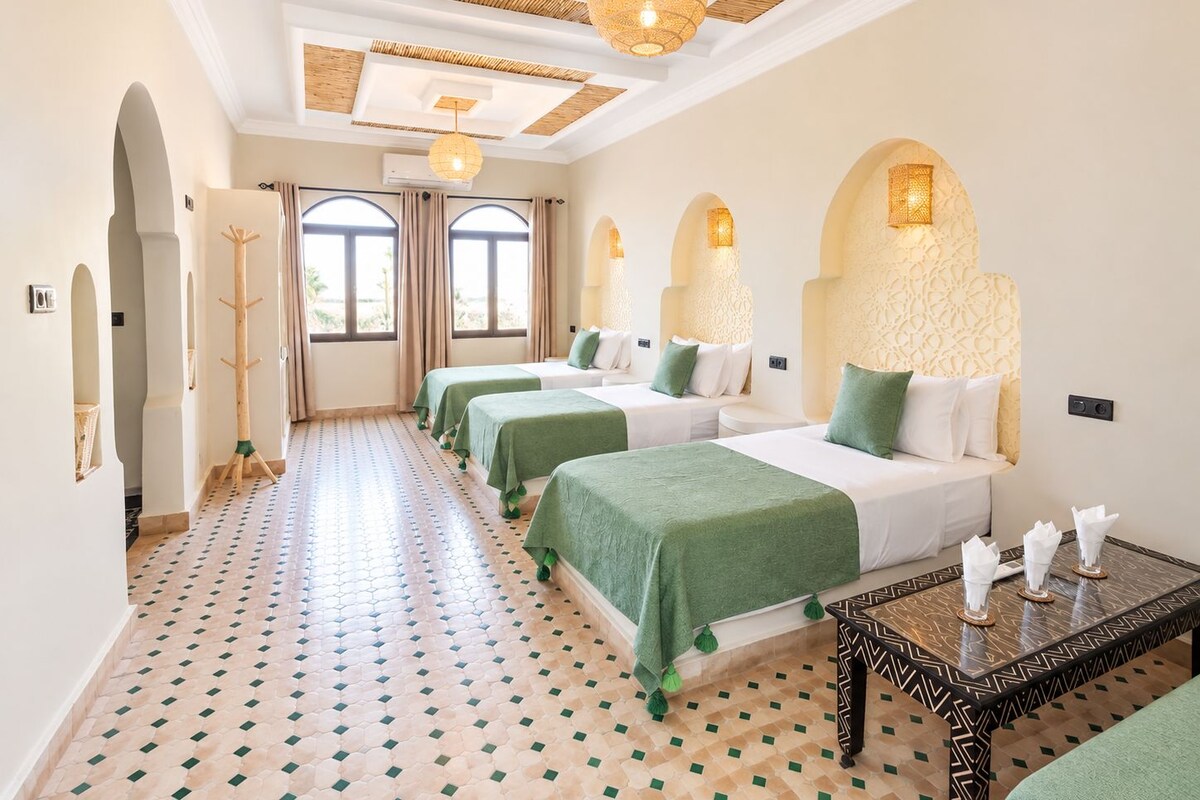 Quarto de hotel com três camas, piso estampado e corredor com um porta-roupas.