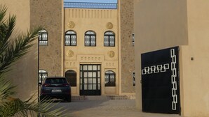 A building with a large black gate, a car parked in front, and a clear blue sky. - Riad La Luna (Merzouga)