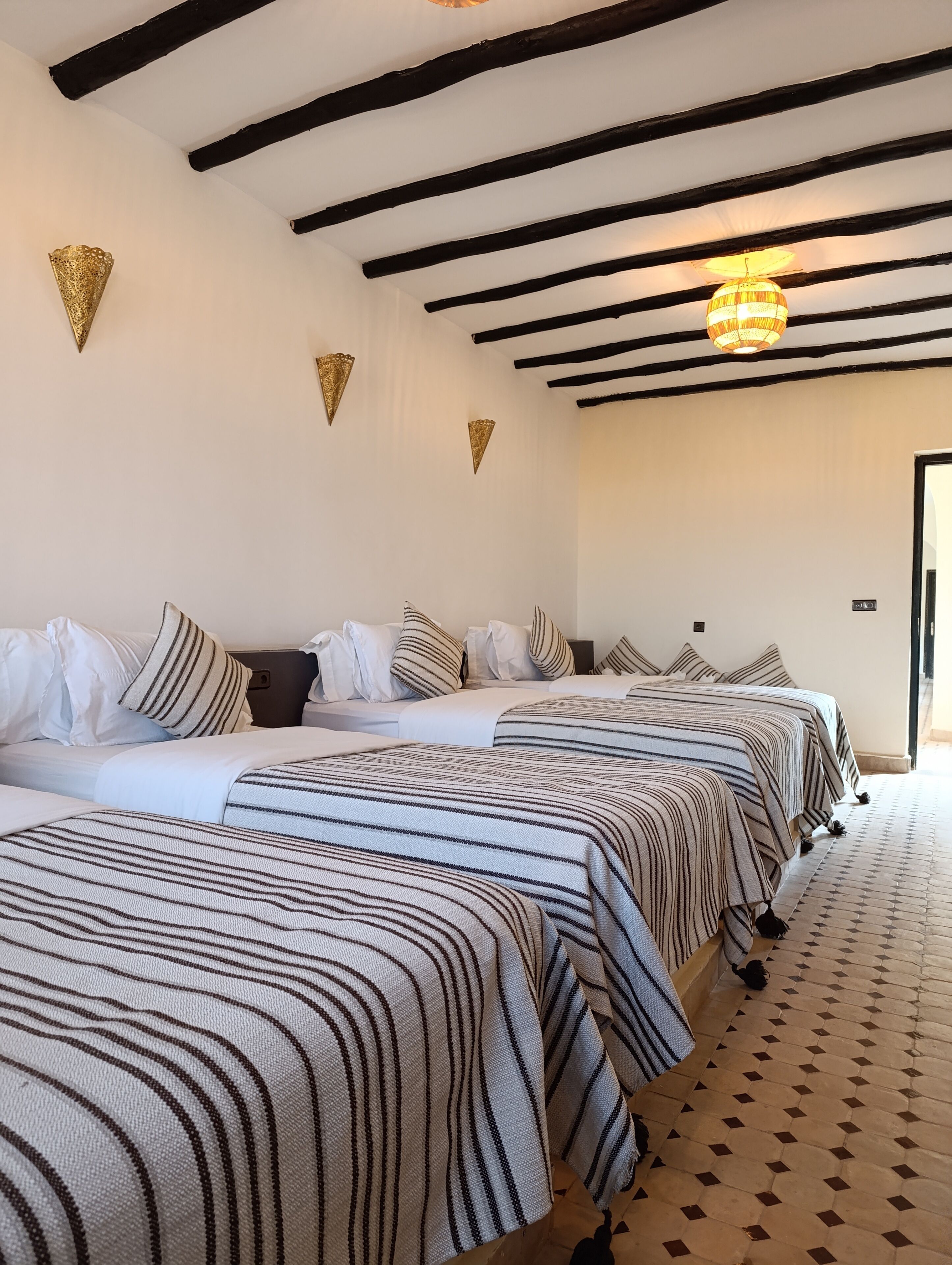 Une chambre d’hôtel avec deux lits, une literie à rayures, un sol à motifs et un plafond avec des poutres apparentes.
