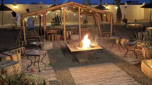An outdoor patio area with a fire pit, seating arrangements, and string lights. - Riad La Luna (Merzouga)