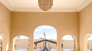 A room with a patterned floor, a hanging light fixture, and a view through an archway. - Riad La Luna (Merzouga)