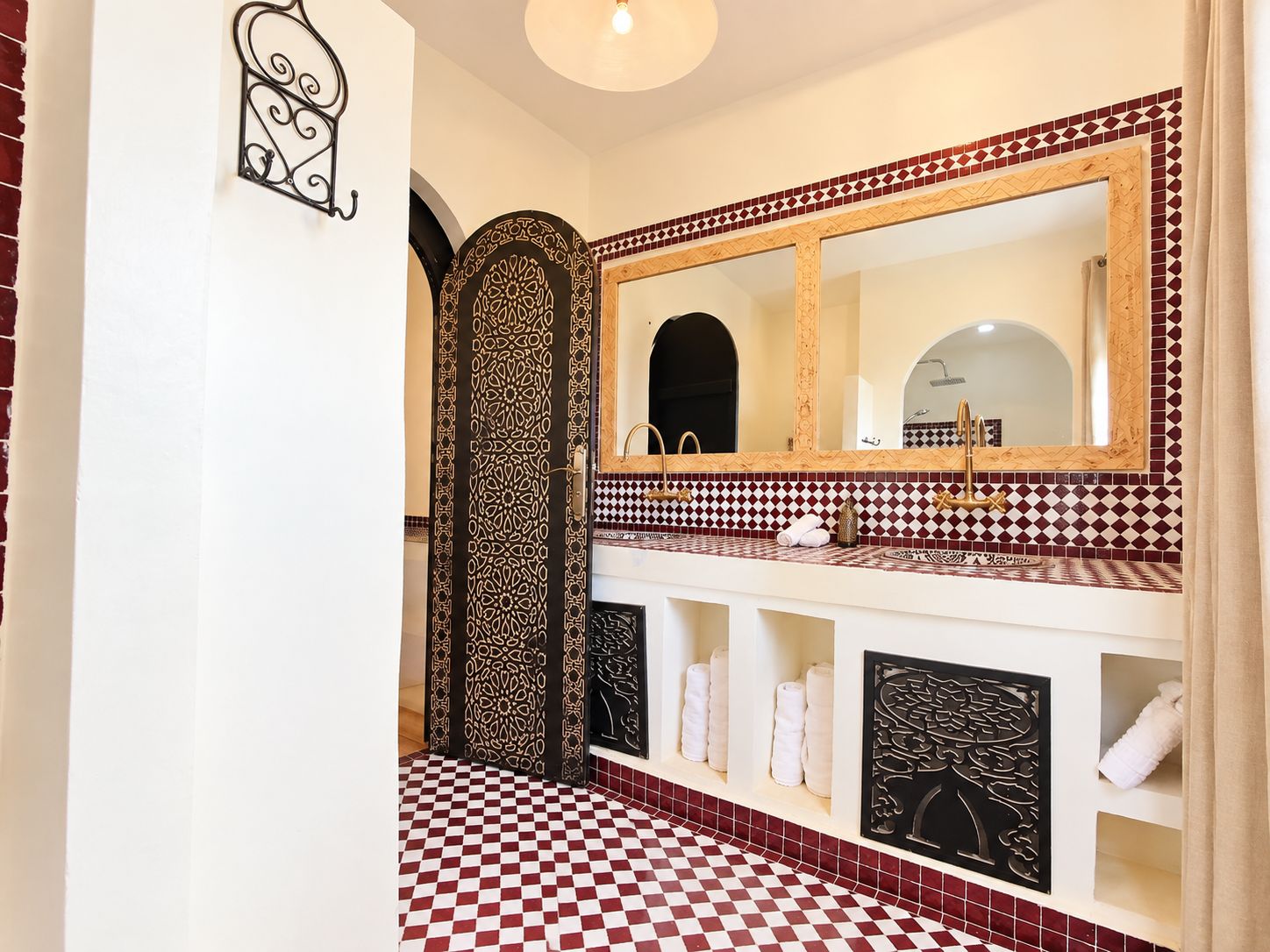 A bathroom with a checkered floor, a large mirror with a decorative frame, and a vanity with a patterned backsplash.