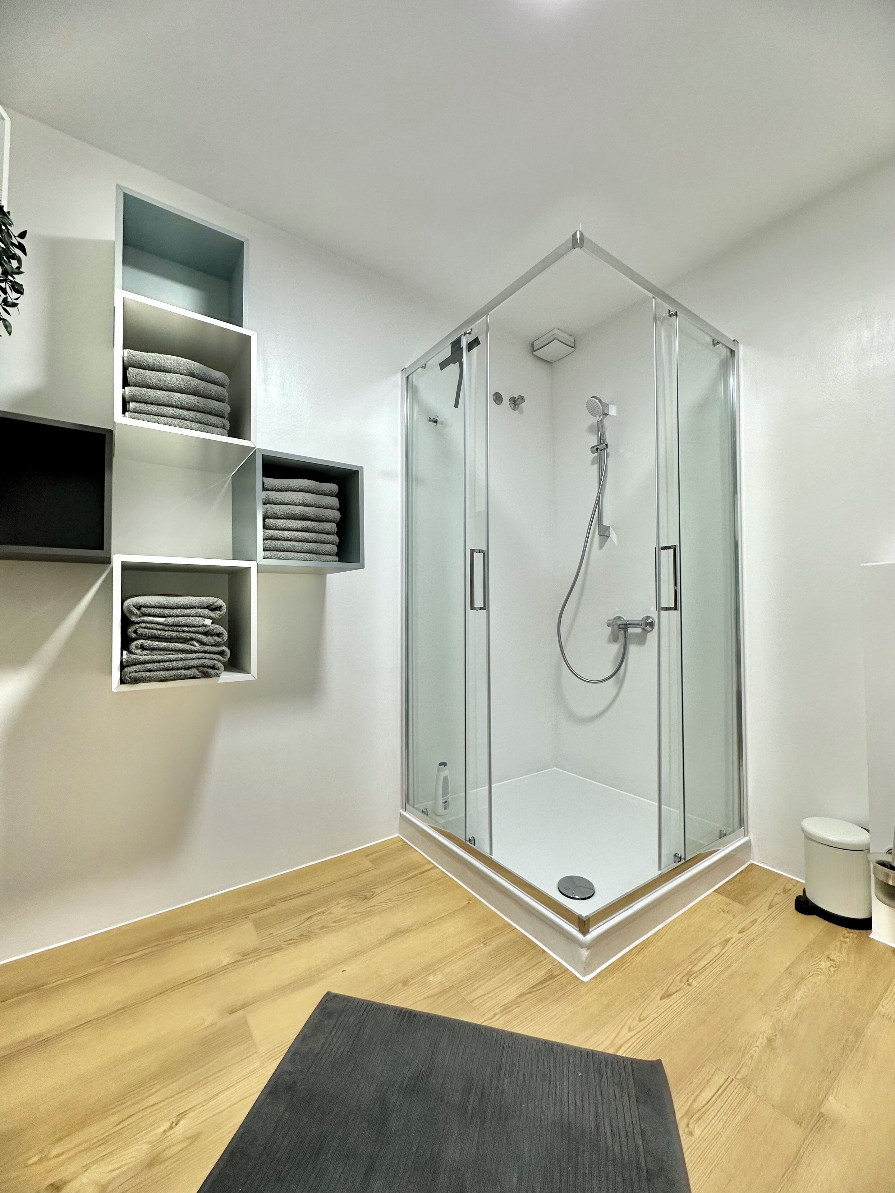 A modern bathroom with a glass-enclosed shower, wooden flooring, and built-in towel racks.