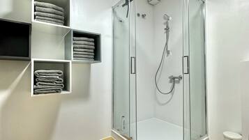 A modern bathroom with a glass-enclosed shower, wooden flooring, and built-in towel racks.