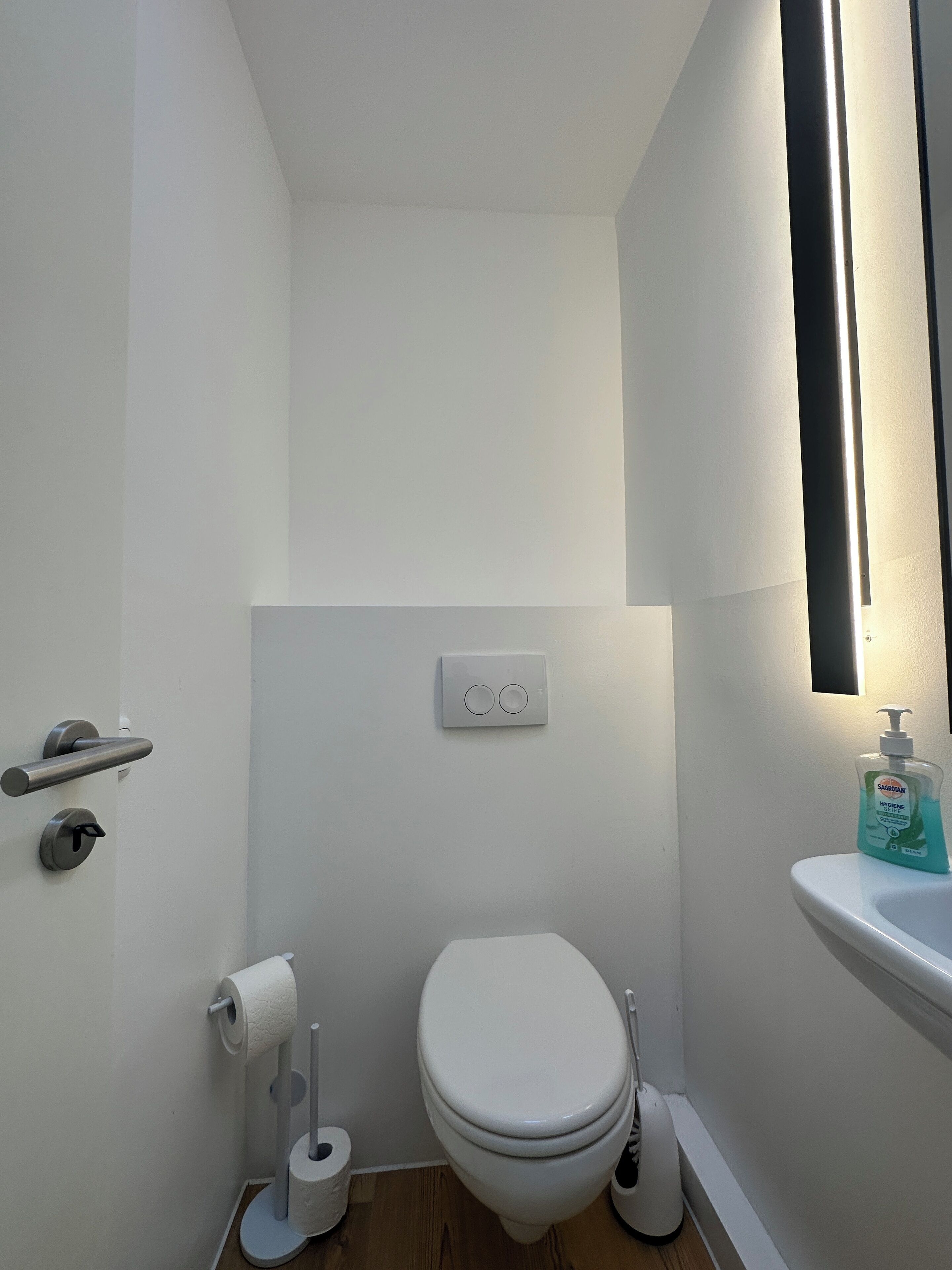 Een kleine, witte badkamer met een toilet, een handdroger, een papieren handdoekdispenser en een zeepdispenser bij een wastafel.