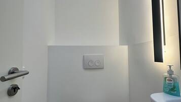 Een kleine, witte badkamer met een toilet, een handdroger, een papieren handdoekdispenser en een zeepdispenser bij een wastafel.
