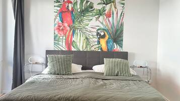 Ein Schlafzimmer mit einem großen Bett, zwei Kissen, einer Wandleuchte und einem Wandbild mit tropischem Motiv.