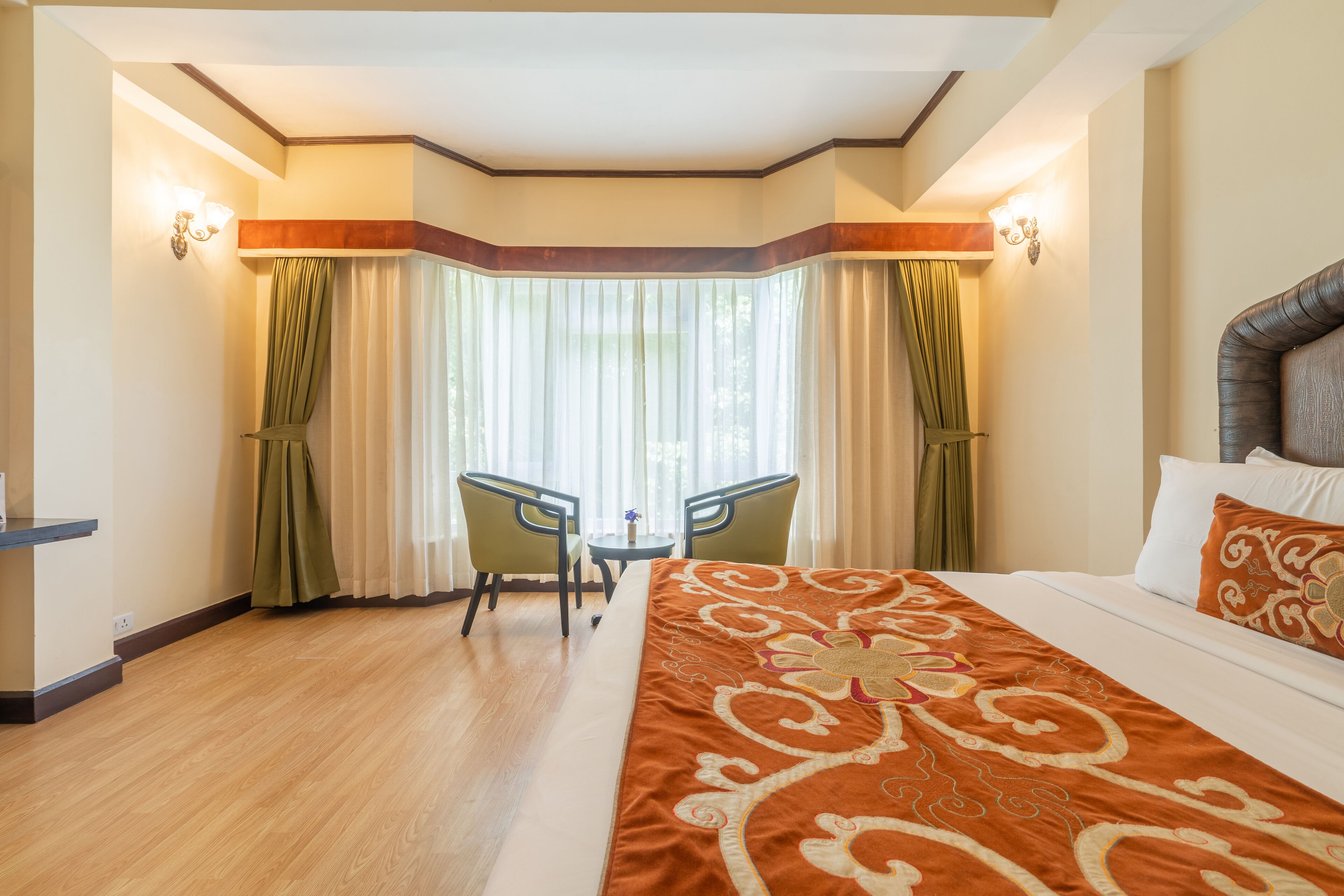 A hotel room with a large bed, a desk with two chairs, and a view of the outdoors through large windows.