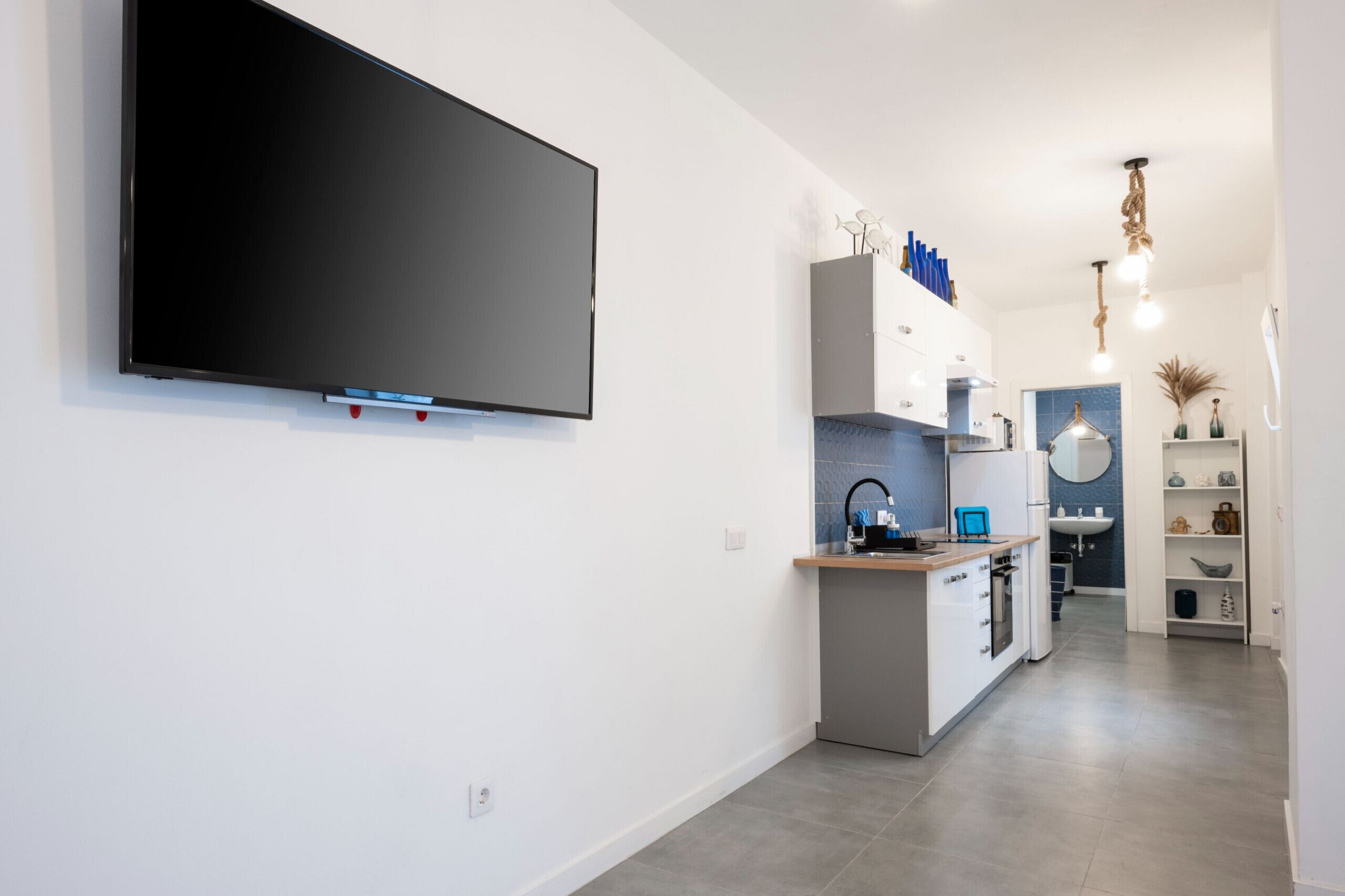 A modern kitchen with a flat-screen TV mounted on the wall, a built-in oven, and a sink.