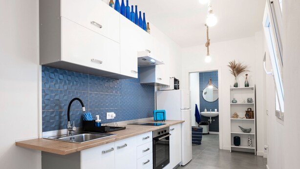 A modern kitchen with white cabinets, a blue backsplash, and a wooden countertop.