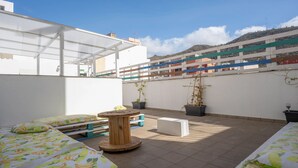 A rooftop terrace with two beds, a wooden table, and potted plants.