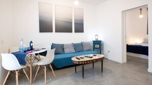A modern living room with a sofa, coffee table, and dining area. There are three wall-mounted artworks above the sofa.