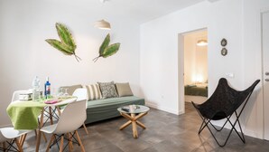 A modern living room with a dining table, chairs, a sofa, a unique black chair, and decorative wall art.