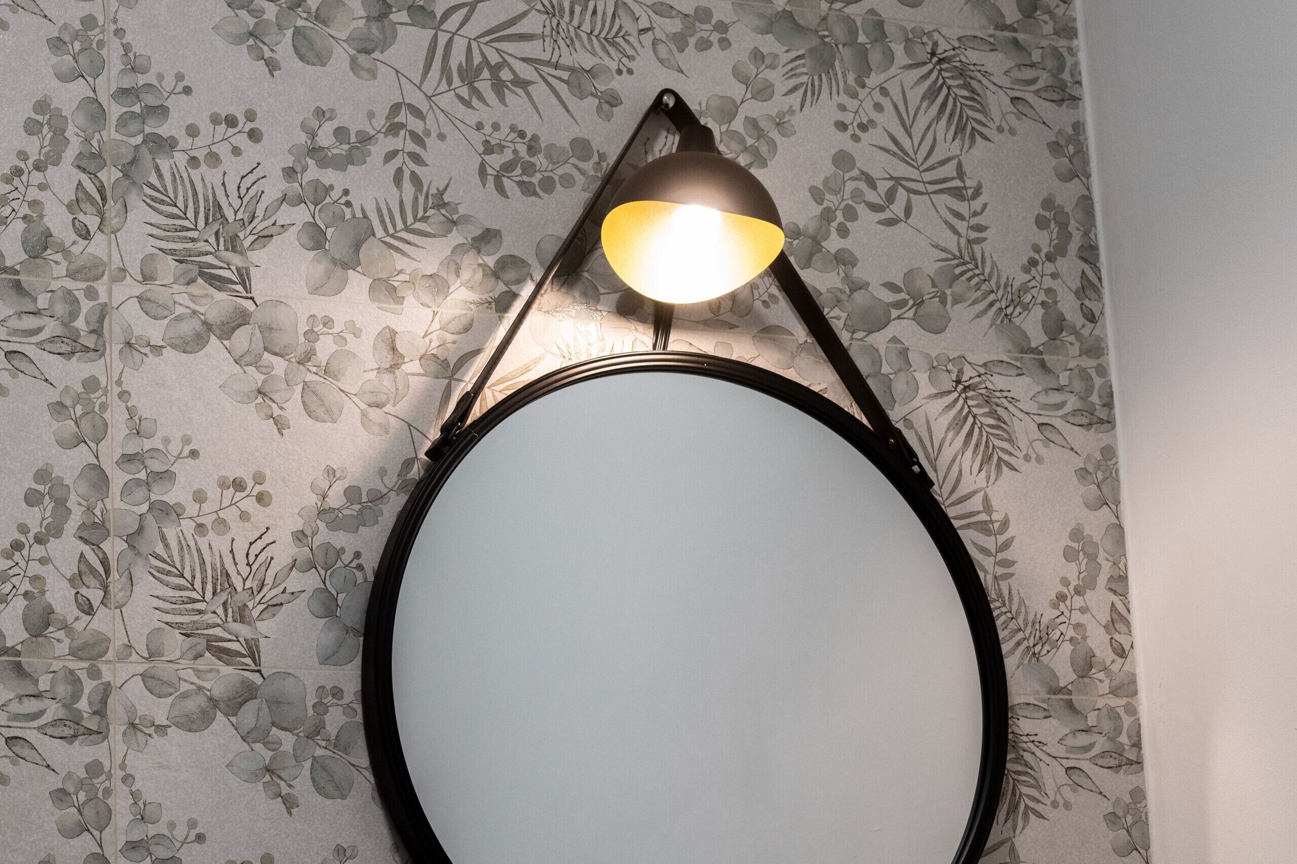 Un miroir mural avec un cadre noir et un luminaire placé au-dessus.