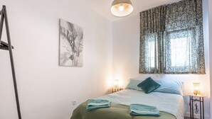 A bedroom with a bed, two bedside lamps, a green blanket, and a window with patterned curtains.