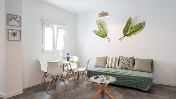 A modern living room with a green sofa, white chairs, a small round table, and a dining area with a table and chairs.