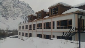 A multi-story building with a staircase on the right side, surrounded by snow-covered ground and mountains in the background. - The Nun Kun Residency Kargil (Kargil)