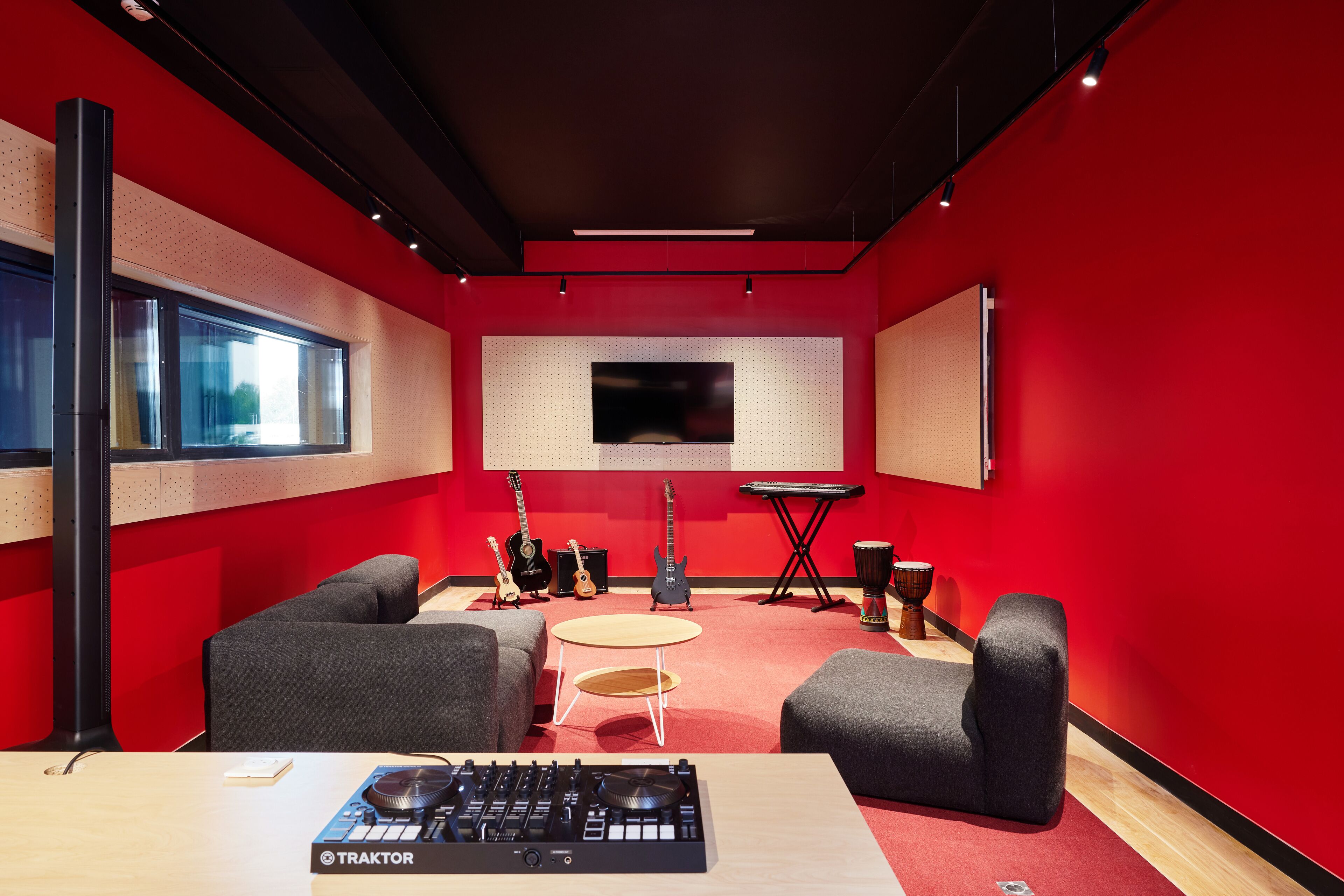 Un studio d’enregistrement aux murs rouges, équipé d’une console de mixage et d’instruments de musique.
